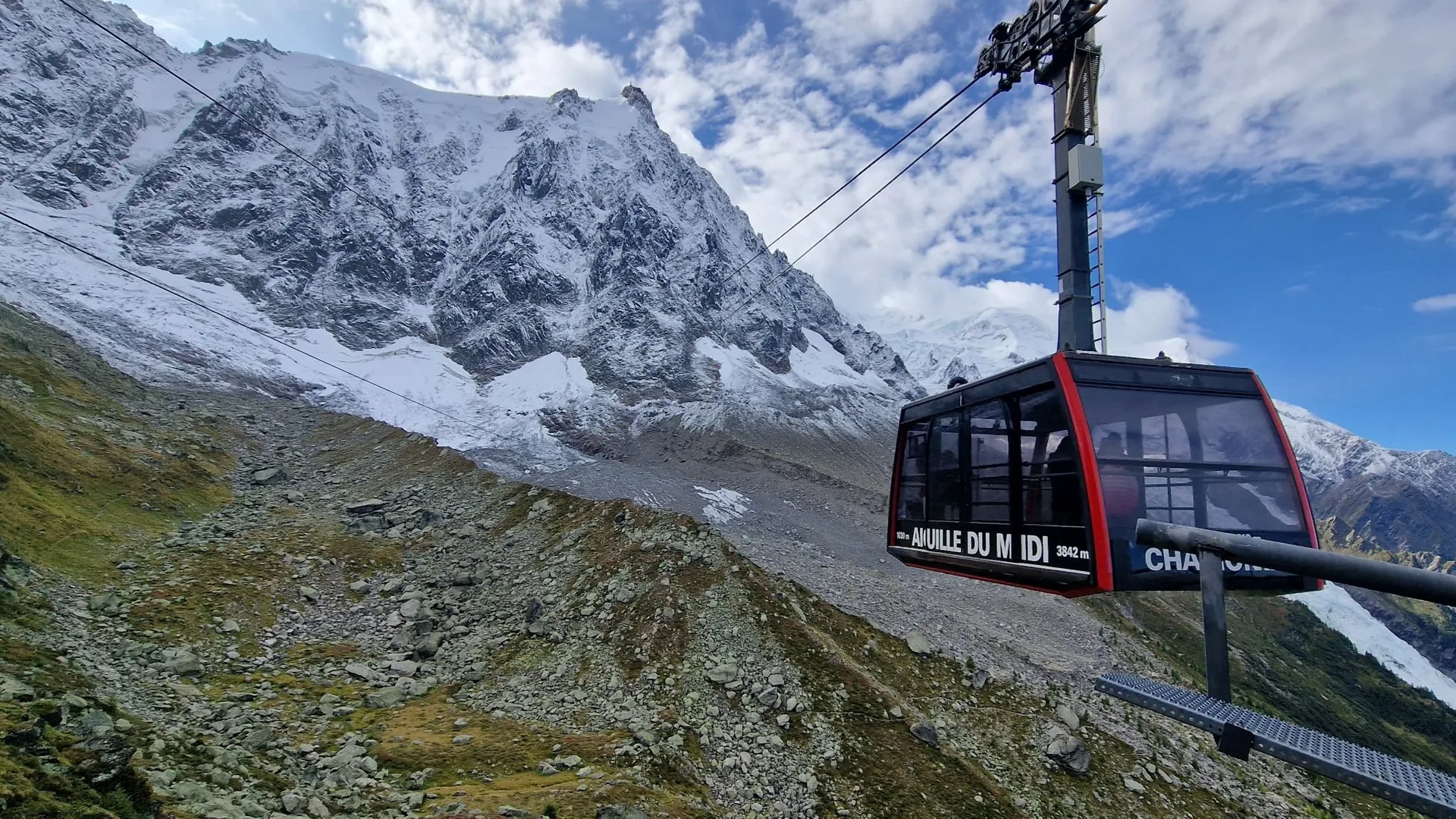 The red Aiguille du Midi cable car cabin climbing above the valley with the snow-covered Mont Blanc massif behind, from the guided Chamonix day listing
