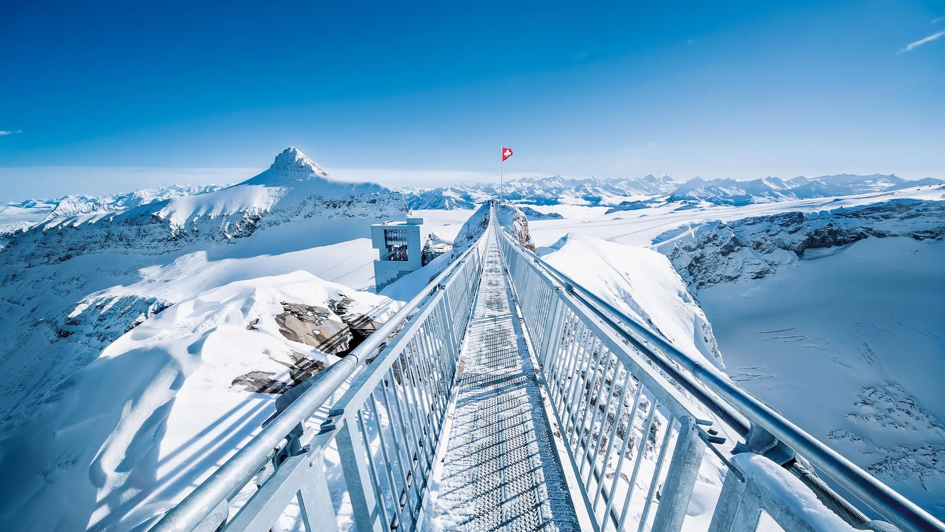 The Peak Walk suspension bridge across the snow at Glacier 3000 under a blue sky, from the Glacier 3000 day listing