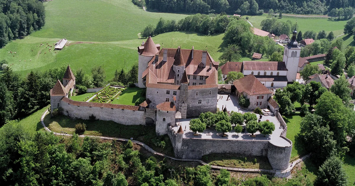 The castle and medieval village of Gruyères on a green hill above the Fribourg countryside, seen from the air